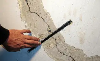 A wall with a large crack is being inspected by a professional in Fort Worth, TX